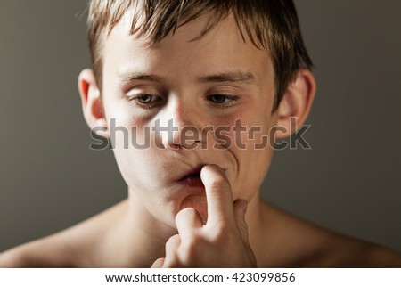 Head and Shoulders Close Up of Young Shirtless Teenage Boy Picking Teeth with Finger or Sucking on Finger While Deep in Thought, Looking Down and to the Side in Studio with Copy Space