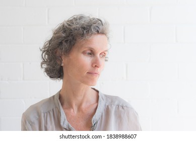 Head and shoulders closeup of natural looking middle aged woman looking away from camera against white background (selective focus)