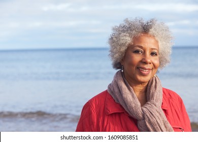 Head And Shoulders Portrait Of Active Senior Woman Walking Along Winter Beach With Sea Behind