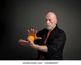 Head and shoulders portrait of bald and bearded senior man with a spiky self massage ball in his hands, self care concept