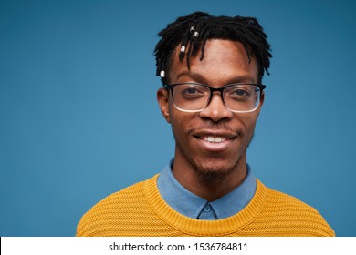 Head and shoulders portrait of contemporary African-American man smiling at camera while wearing bright knit sweater and posing against blue background, copy space
