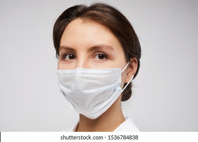 Head And Shoulders Portrait Of Female Doctor Wearing Protective Mask And Looking At Camera Posing Against White Background