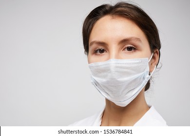 Head And Shoulders Portrait Of Female Doctor Wearing Protective Mask And Looking At Camera Posing Against White Background, Copy Space