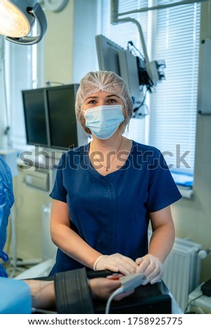 Head and shoulders portrait of female doctor wearing protective mask and looking at camera. Posing against medicalequipment background. Copy space