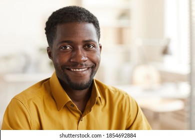 Head and shoulders portrait of smiling African-American man looking at camera while enjoying work in white office interior, copy space
