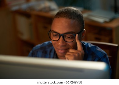 Head and shoulders portrait of smiling Afro-American man wearing eyeglasses browsing Internet while sitting in front of computer, blurred background - Shutterstock ID 667249738