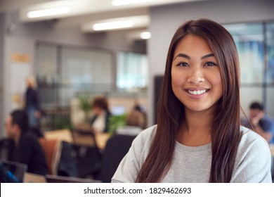 Head And Shoulders Portrait Of Smiling Young Asian Businesswoman  Working In Busy Modern Office