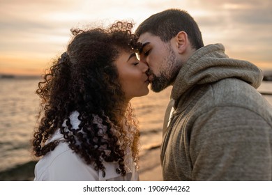 Head and shoulders portrait of young beautiful couple in love kissing at sunset in winter seaside resort with cloudy sky. Two millennials in vacation travel manifesting their heart sentiments outdoor - Shutterstock ID 1906944262