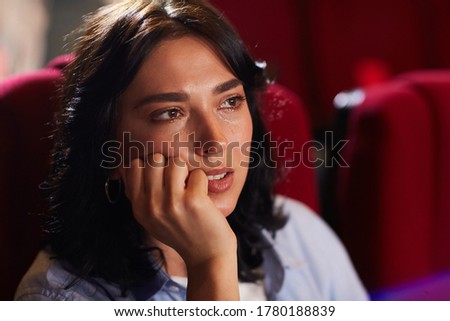 Head and shoulders portrait of young woman crying in cinema while watching sad drama movie, copy space
