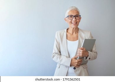 Head And Shoulders View Of Beautiful Older Woman With Short Grey Hair And Beige Jacket Against Grey Background. Business Woman With Glasses Smiling. Portrait Of Beautiful Mature Woman