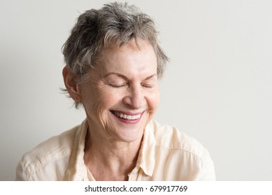 Head And Shoulders View Of Older Woman With Short Grey Hair Laughing With Eyes Closed Against Neutral Background (selective Focus)