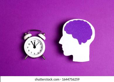 Head silhouette with a purple brain and white alarm clock on a purple background. Epilepsy disease or Alzheimer disease awareness world day.