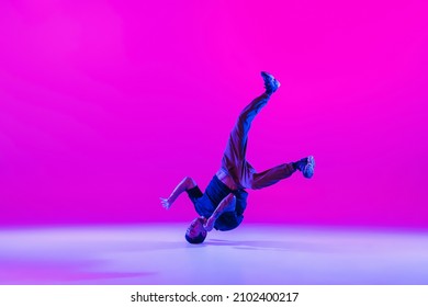 Head spin, moves. Young cool man, guy, dancer training alone isolated over bright magenta background at dance hall in neon light. Youth culture, movement, street style and action. Copy space for ad - Powered by Shutterstock