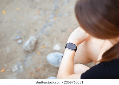 head of Young woman looking at the smart clock checking pulse sitting on the roadside in forest park, health and sport concept, top view - Shutterstock ID 2368760551