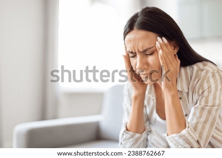 Headache Concept. Young stressed woman suffering from migraine at home, sick millennial female rubbing temples while sitting on couch in living room, feeling unwell, having acute pain, closeup shot Imagine de stoc © 