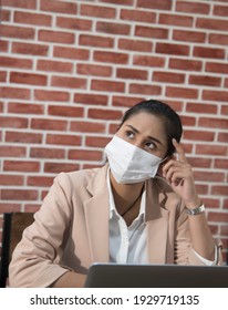 Headache Or Confusion. Portrait Of Young Woman With Surgical Medical Mask Is Sitting And Working On Computer And Holding Her Painful Head Or Thinking. Indoor Working, Medicine And Health Care Concept.