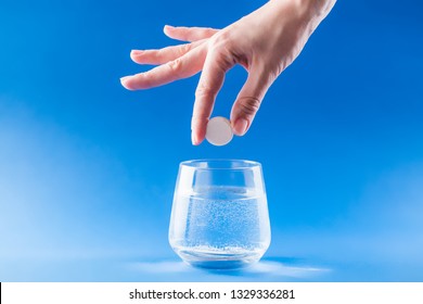 Headache Medicine. Woman Hand Puts Aspirin Into Glass With Water. Health Care Concept With Blue Background.