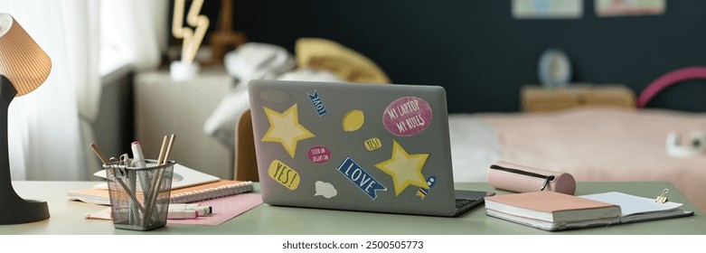 Header background image of open laptop decorated with stickers on desk in childs room with school supplies artistic workspace environment
