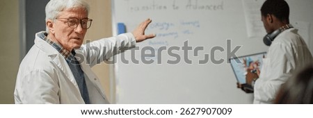 Header image of senior professor teaching medicine in class and pointing at whiteboard with student writing, copy space