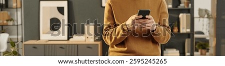 Header image of smiling young man using phone while standing in office and checking messages via internet, copy space