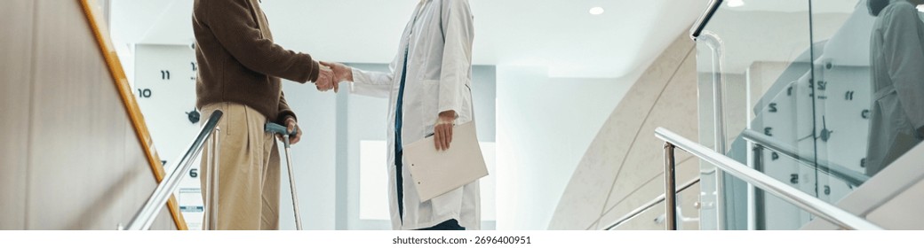 Header of middle aged man with disability using crutches shaking hands with young adult female doctor in white lab coat, standing in modern medical facility near staircase