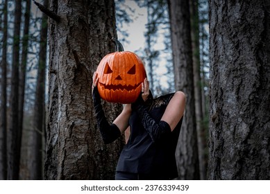 Headless female pumpkin person dressed in black stands in the forest on a gloomy day