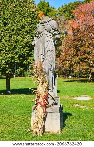 Headless stone statue in fall with fall decor in grass field