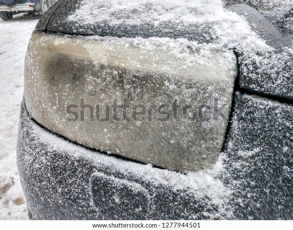 Headlight black car covered with snow and ice.\
Closeup view