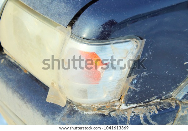 The headlight of\
the car is close-up. The headlight is sealed with an adhesive tape.\
Dirty front of the car.