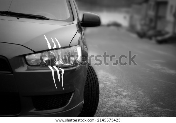 The headlight of a\
car with imitation scratches from claws. Black and white photo of\
the front of the car.