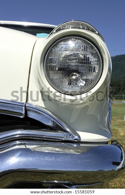 A headlight\
and chrome bumper of a classic\
car.