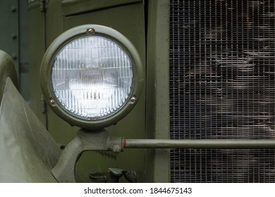 Headlight And A Fragment Of The Cockpit And Radiator Of An Old Truck From The Second World War. The Casing Is Painted In A Protective Green Color. Background. Texture.