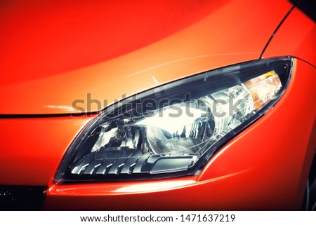 Headlight of an orange or red sports car, close up detail of the hood, fender, bumper and light, copy space 