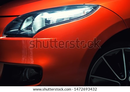 Headlight of an orange or red sports car, close up detail of the side view of the car with fender, bumper, wheel and light