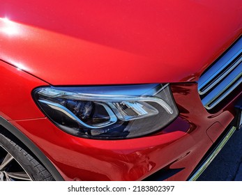 Headlight Of A Red New Shiny Car. Closeup View. Fragment Of A New Bright Red Sports Car With A Xenon Headlight