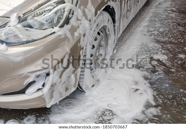 Headlight and wheel of a passenger\
car in shampoo foam close-up, car wash service, vehicle\
care