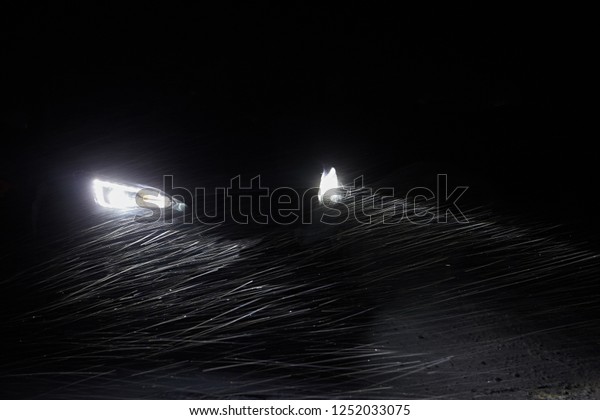 The\
headlights of the car brightly illuminate the road and flying\
snowflakes in the air against the black\
night
