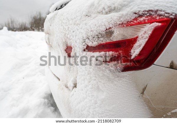 Headlights and trunk of a car are covered in snow,\
outdoors, on a winter day.\
