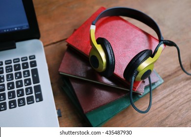 headphone and laptop on wood table , Enjoys digital music listening,Layout of comfortable working space on wooden, internet laptop headphone phone notepad pen eyeglasses laying on it
