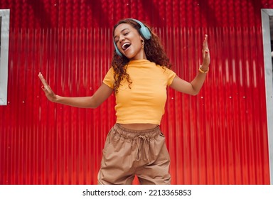 Headphones, black woman and happy dance in city against red building background. Music, dancing and carefree female dancer in Brazil laughing, singing and streaming audio or radio on wireless headset - Powered by Shutterstock
