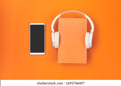 Headphones with book and smartphone on orange background.