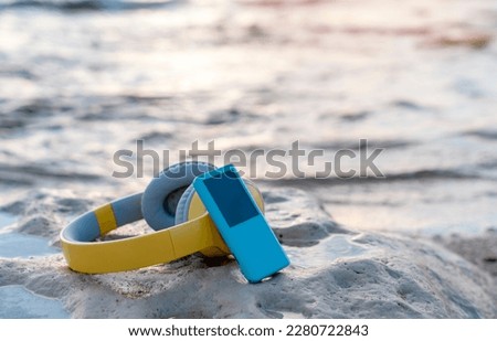 Headphones and MP3 player on the beach on the sand near the sea at sunset.  Take music or book on a journey, listen to the music of nature. Copy space