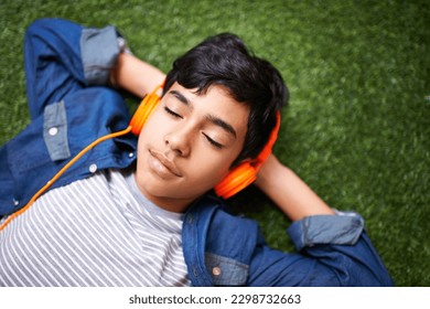 Headphones, music and boy relax on grass with eyes closed outdoors on holiday, free time and weekend. Calm, peace and face of kid in garden listening to song, track and streaming audio for happiness - Powered by Shutterstock