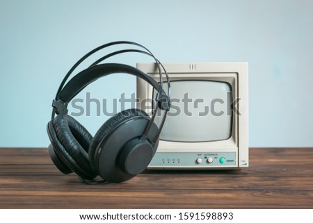 Headphones near a small old monitor on a wooden table on a blue background. Technique for sound and video reproduction.