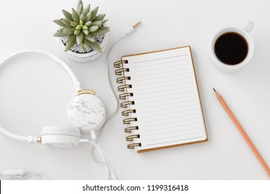 Headphones with notebook, pencil, coffee cup on white desk