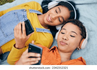 Headphones, phone and lgbt couple on picnic on grass, relax, technology and streaming service in nature. Cellphone, listening to music and happy lesbian women on blanket in garden together from above - Powered by Shutterstock