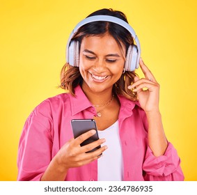 Headphones, phone and young woman in a studio listening to music, playlist or radio and networking. Happy, cellphone and female model from Mexico streaming a song or album by yellow background. - Shutterstock ID 2364786935