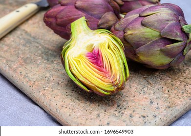 Heads of raw fresh purple romanesco artichoke vegetable ready to cook on marble cutting board