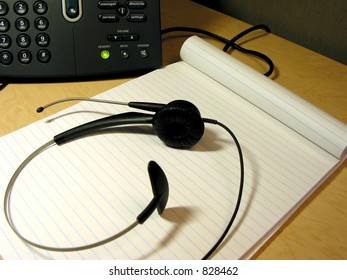 Headset and notepad on the office desk with IP phone in the background