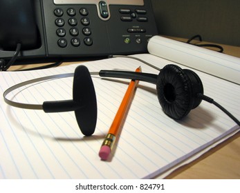 Headset, pencil and notepad on the office desk with IP phone in the background
